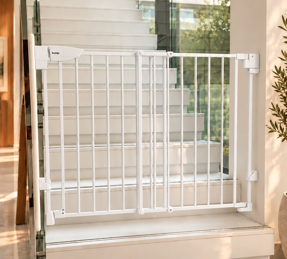 White Bumpr metal safety gate fitted at the foot of a white staircase with glass balustrade